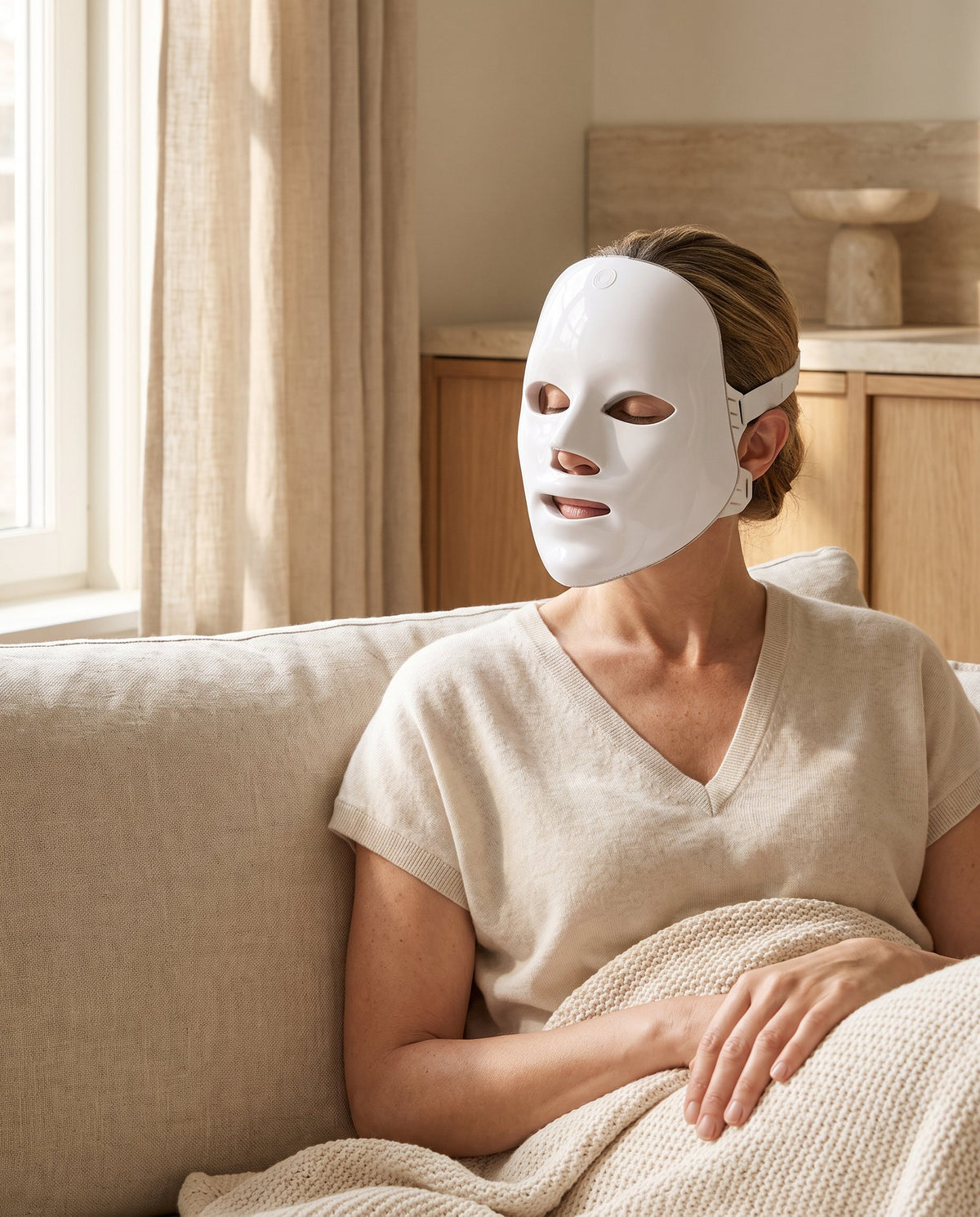 Femme assise sur un canapé en lin, portant un masque LED visage blanc