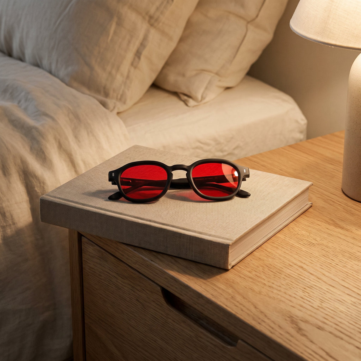 Lunettes à verres rouges posées sur un livre, table de chevet, lumière du soir